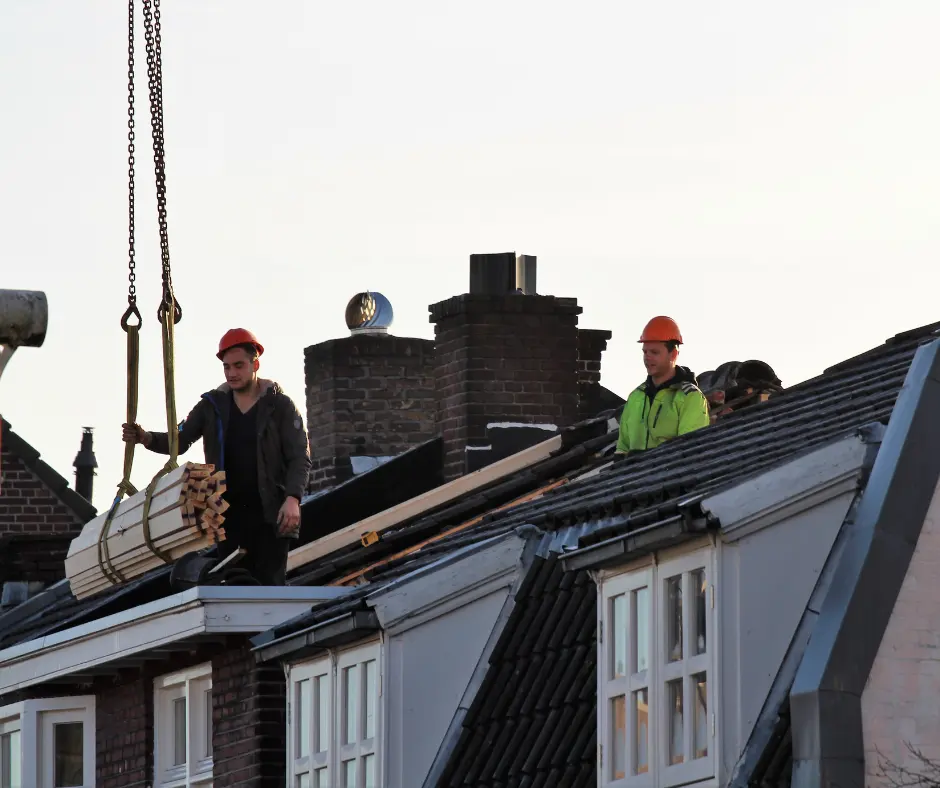 roofers in the roof doing roofing construction. materials are being lifted by a machine