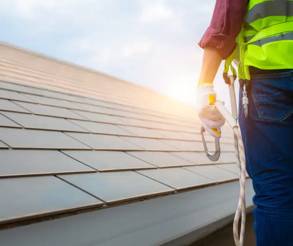 roofer wearing a harness in a roof doing roofing construction. sunrise in the background.