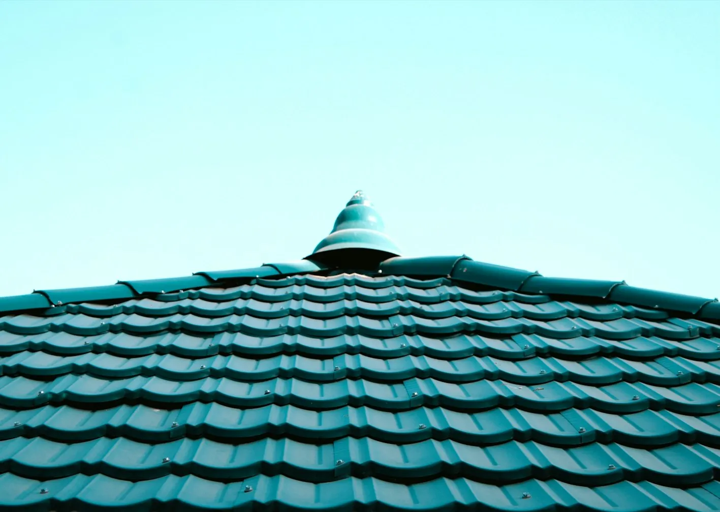 view of a teal, textured rooftop with a decorative peak against a light blue sky.