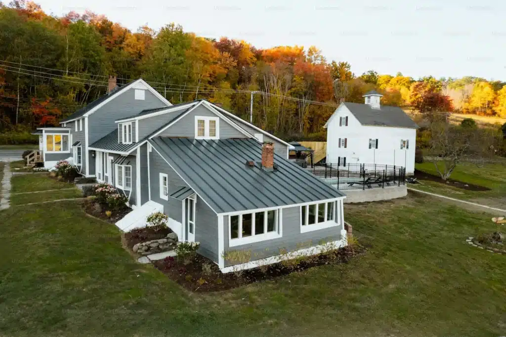 modern gray house with a metal roof and a white cottage in a scenic landscape adorned with vibrant autumn foliage.