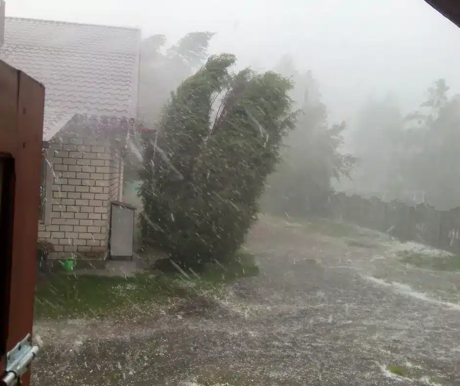 A severe hailstorm with heavy rain and wind bending trees, impacting a house and yard.