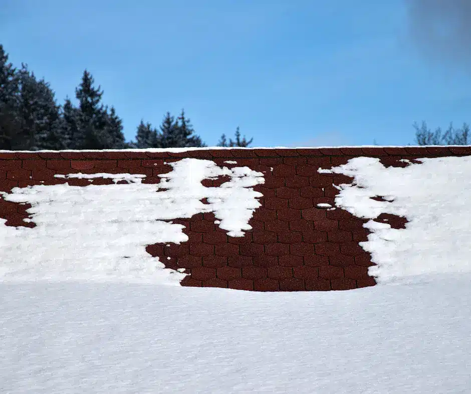 Red shingle roof partially covered in snow with a forest in the background. Best shingles roofs for cold climates