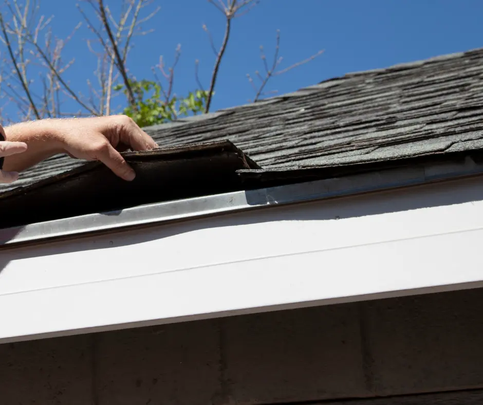 A roofer lifts a damaged shingle to inspect the roof's underlying structure.