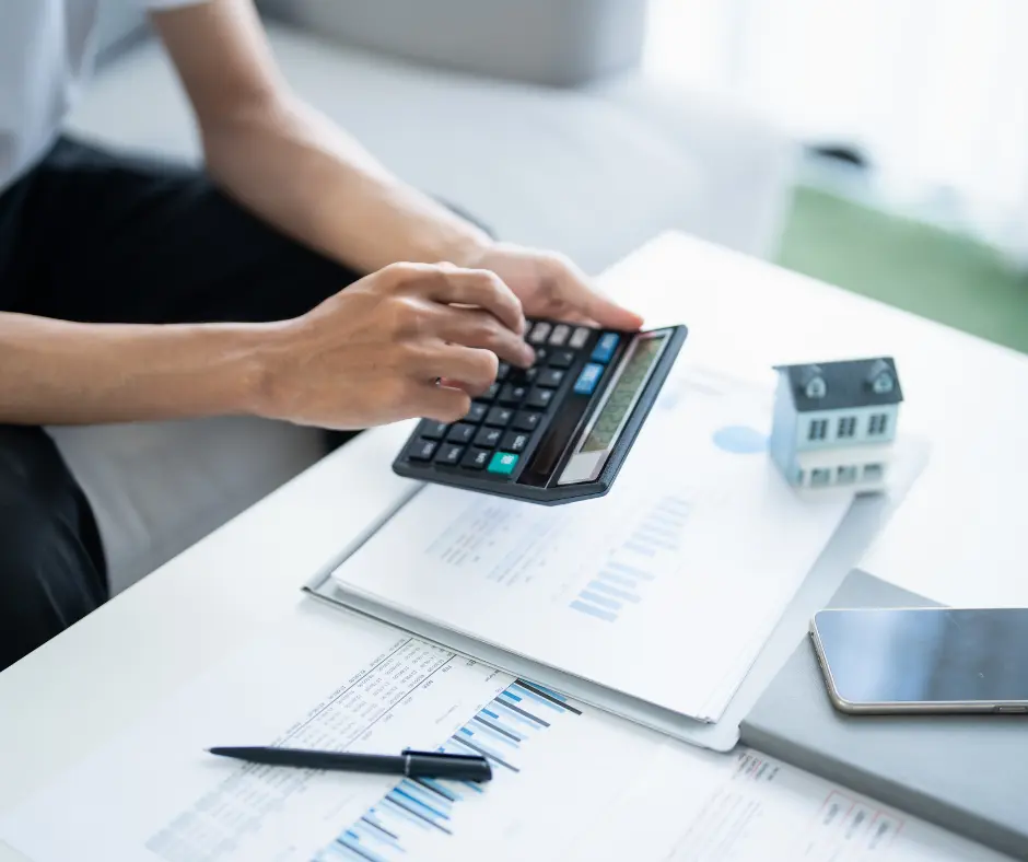 Roof financing faqs: Person calculating finances for roof financing with house model and paperwork.