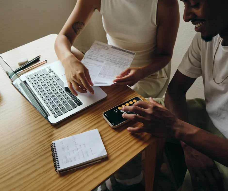 Two people reviewing financial documents and using a calculator at a desk with a laptop.
