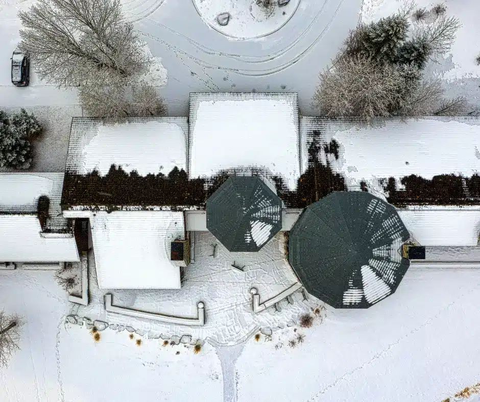 Aerial view of a house roof covered in patchy snow, it needs winter roof inspections