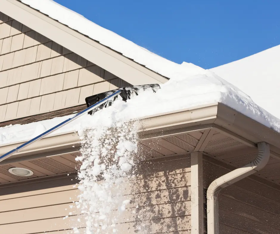 Person using a roof rake to pull snow off a house roof.