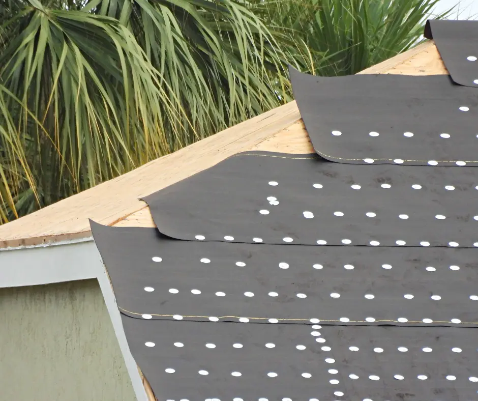  Black roofing underlayment sheet dotted with white fasteners on a roof.