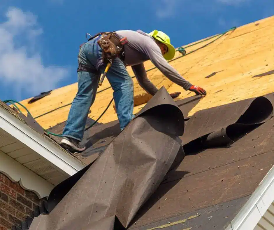 Roofer removing old black felt underlayment from a roof deck.