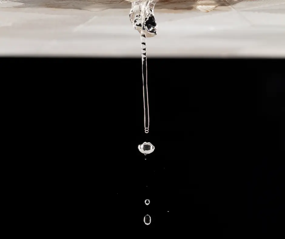 Single drop of water falling from an active roof leak.