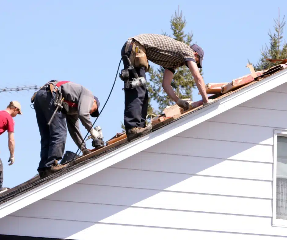 Roofing Crew installing roofing materials on a white-sided house roof.