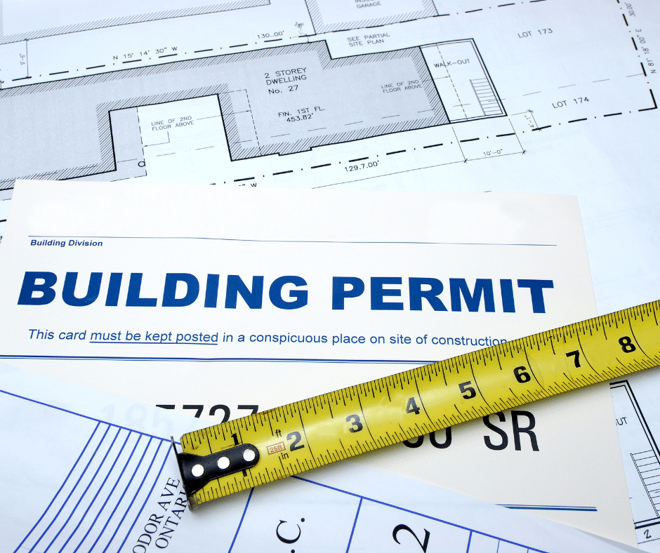 A City of Winnipeg building permit document placed over architectural blueprints with a yellow measuring tape.