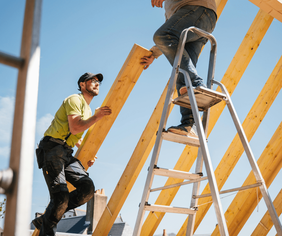 Professional roofing crew members working together on a wooden roof frame under a clear blue sky.